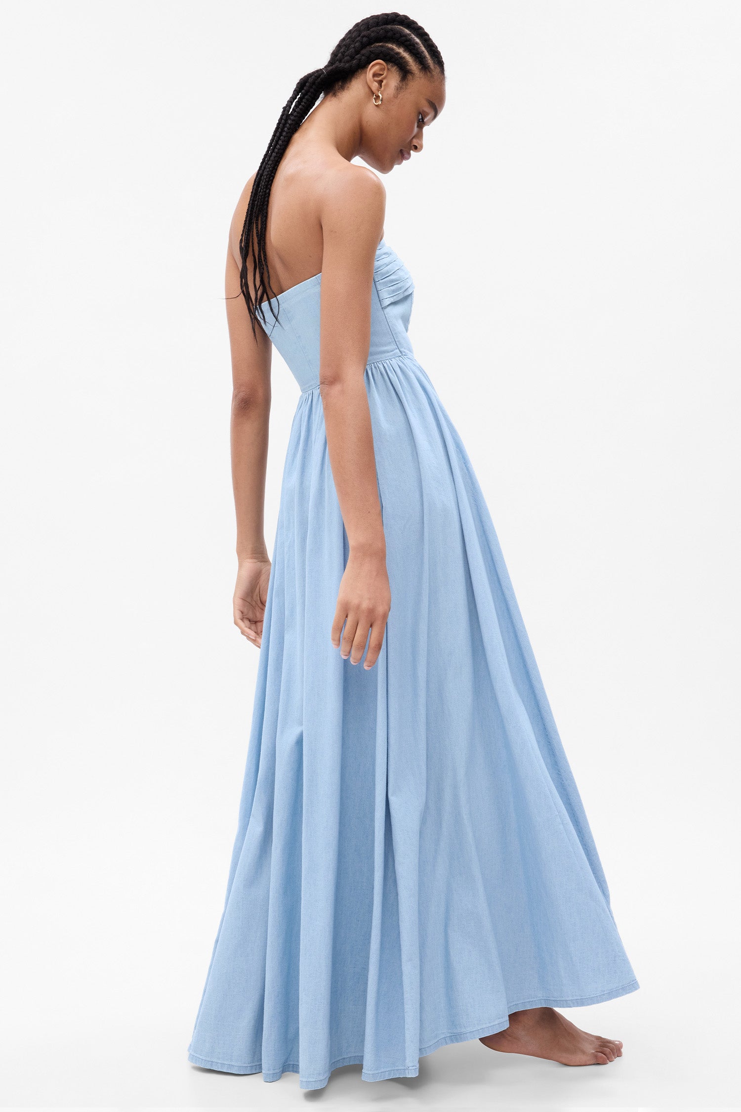 Side image of model wearing blue denim strapless maxi dress with corset top and tiered skirt