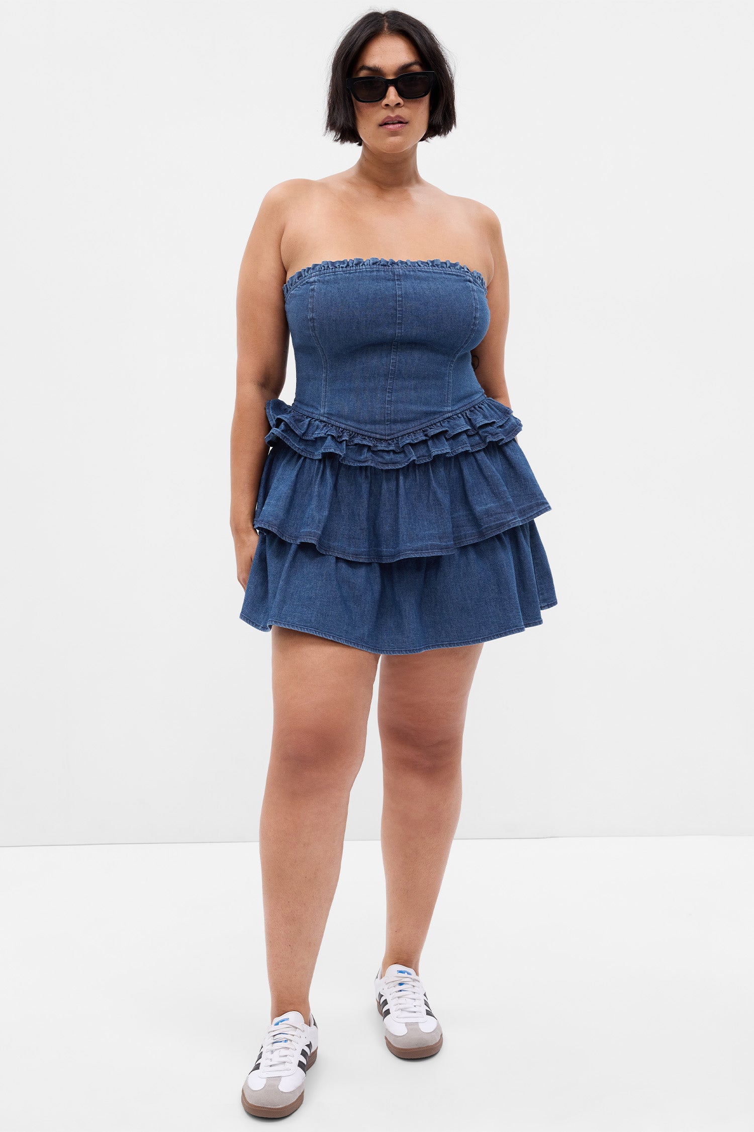 Model wearing blue denim mini dress with corset top and ruffle skirt