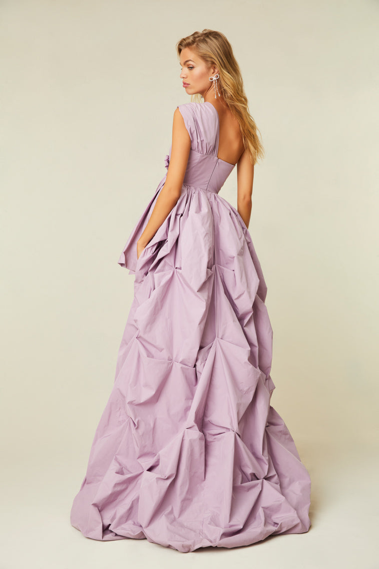 Lavender gown with a one shoulder, high-to-low silhouette that features a ruched bodice, a rosette detailing, and crystals.