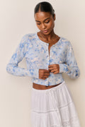 Woman wearing a light blue floral cardigan over a white skirt against a beige background