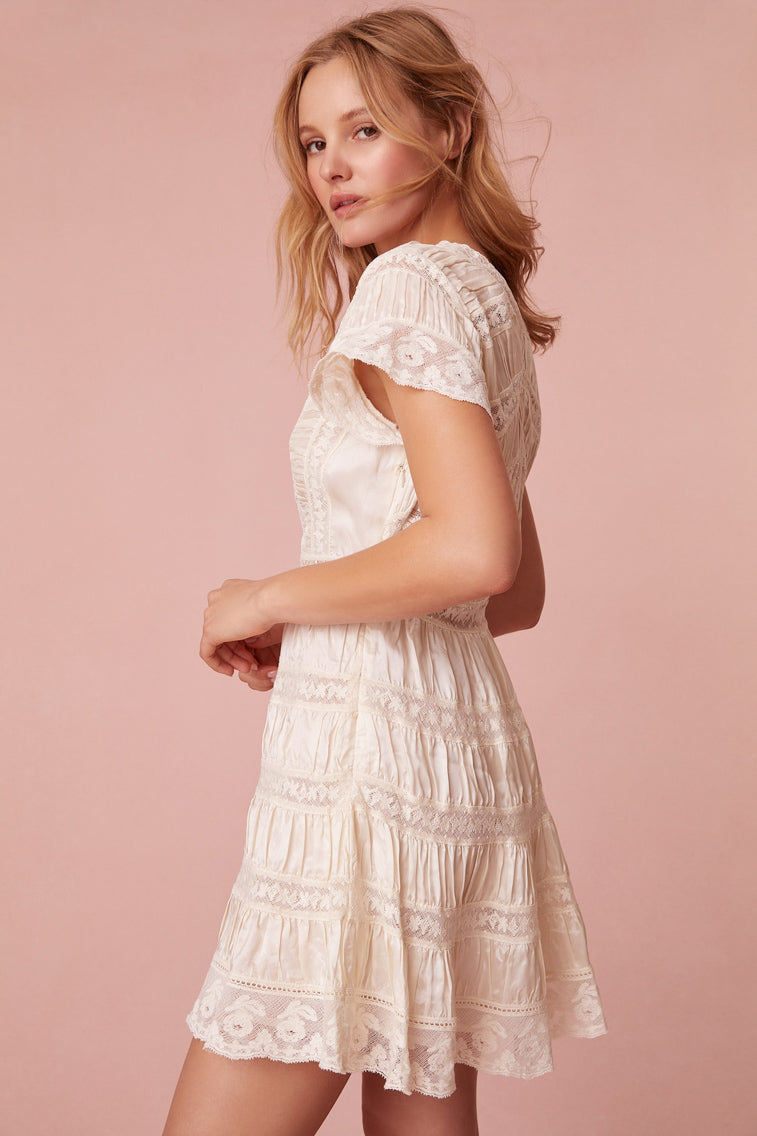 White mini dress designed with a viscose habotai fabric with vintage-inspired laces and textural shirring details all over. Features sweet flutter sleeves, a v-neckline, lace insets throughout, and a side zipper.