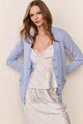 Woman wearing a light blue cardigan over a striped skirt set against a beige background