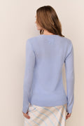 Woman wearing a light blue sweater with a bow detail on a beige background