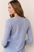 Woman wearing a light blue sweater with a bow detail on a beige background