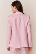 Woman wearing a pink blazer and pants against a plain background