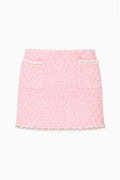 A light pink tweed mini skirt with two front patch pockets, trimmed with sparkling silver rhinestones along the pocket edges and hem, shown against a plain white background.