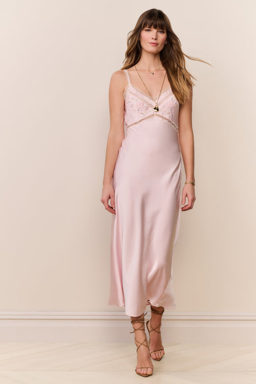 woman wears pink silk gown with lace detailing against beige background