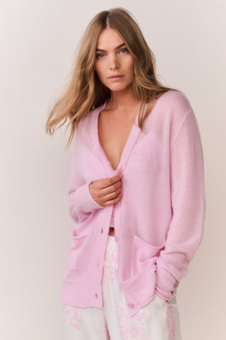 Pink cardigan worn by a woman in pink and white patterned pants and top on a plain background