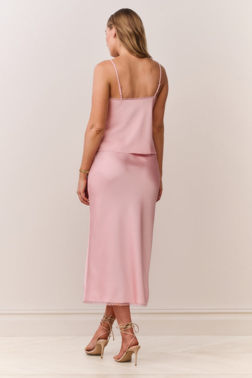 Woman wearing a pink satin cami and matching skirt with thin straps on a plain background