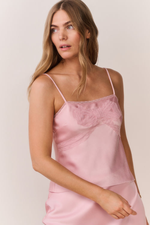 Woman wearing a pink satin slip cami and matching skirt against a plain background