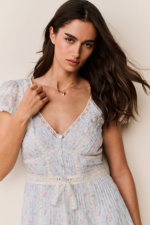Woman wearing a blue floral dress with ruffled against a plain background