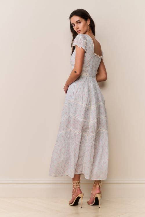 Woman wearing a blue floral dress with ruffled against a plain background