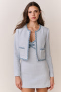 Woman wearing a light blue tweed jacket with decorative trim and matching mini dress on a plain background