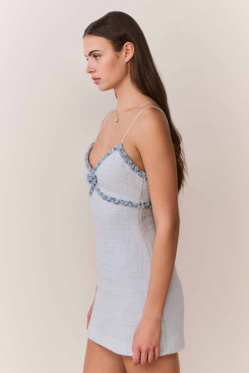 Woman wearing a light blue tweed dress with thin straps on a beige background