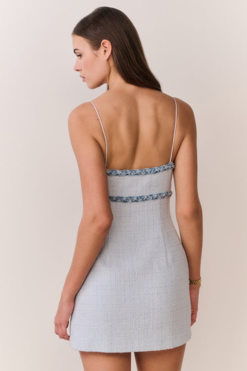 Woman wearing a light blue tweed dress with thin straps on a beige background