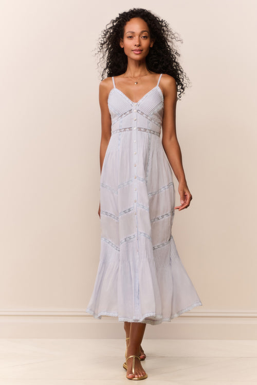 Woman wearing a light blue dress with intricate detailing on a plain background