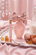Pink travel perfume spray with bow and gold cap on a satin tray with candies.