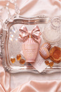 Close-up of pink perfume bottle with bow on a satin cloth with amber candies