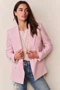 Woman wearing a pink blazer over a ribbed top and blue jeans against a plain background
