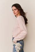 Woman wearing a light pink sweater and blue jeans with lace details against a beige background