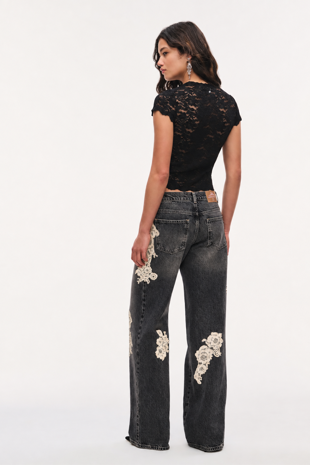 Black wide-leg jeans with cream lace applique on front panels and pockets.