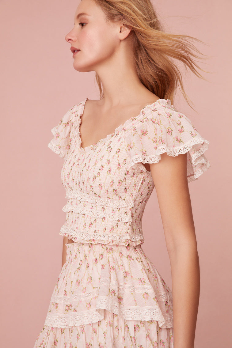 Slightly cropped, the top features short puff sleeves with lace trimming, a sweetheart neckline, and a smocked bodice.