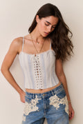 Woman wearing a white and blue stripe lace-up top with thin straps and denim pants with lace details against a beige background