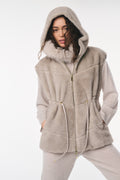 Woman wearing a beige hooded jacket with fur trim on a white background