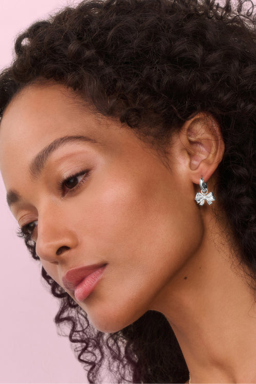 Close-up of a woman wearing earrings with a pink background