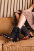 Person wearing brown suede fringe ankle boots sitting on a brown couch.