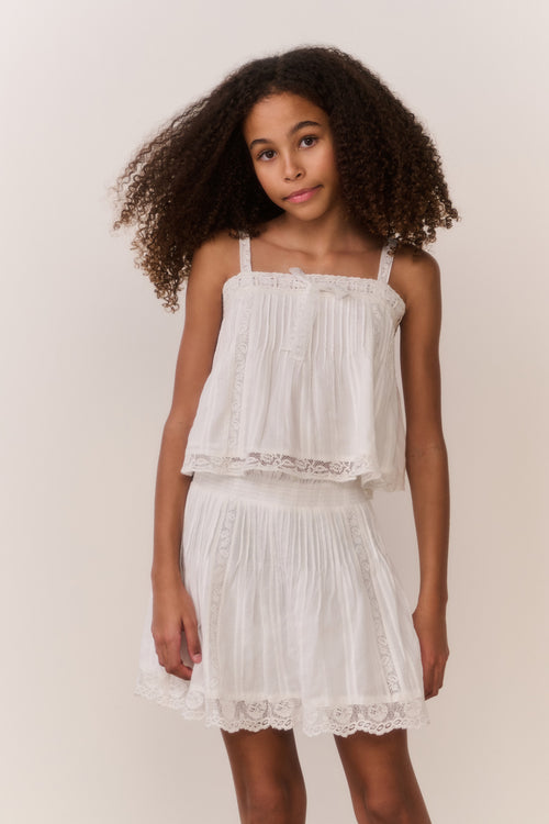 Tween girl wearing white lace trim camisole and matching skirt against white background