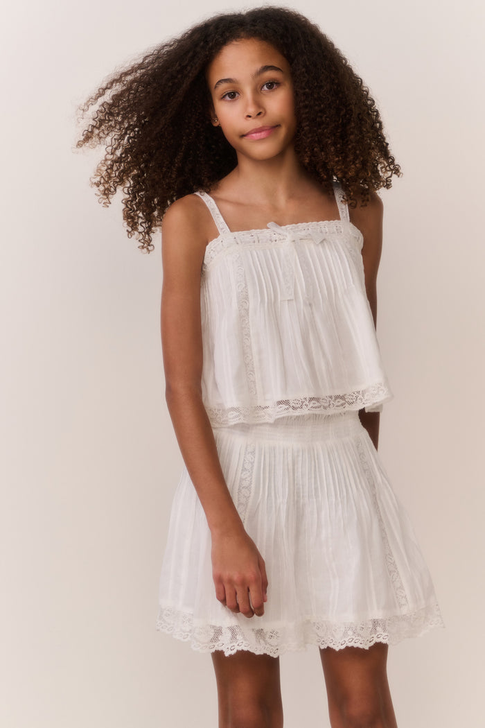 Tween girl wearing white lace trim camisole and matching skirt against white background