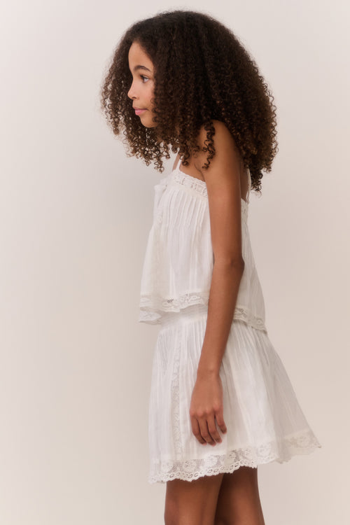 Tween girl wearing white lace trim camisole and matching skirt against white background