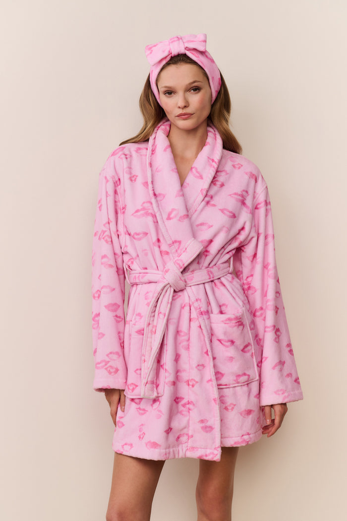 Woman wearing a pink robe with flamingo pattern and matching headband against a beige background