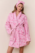 Woman wearing a pink robe with flamingo pattern and matching headband on a beige background