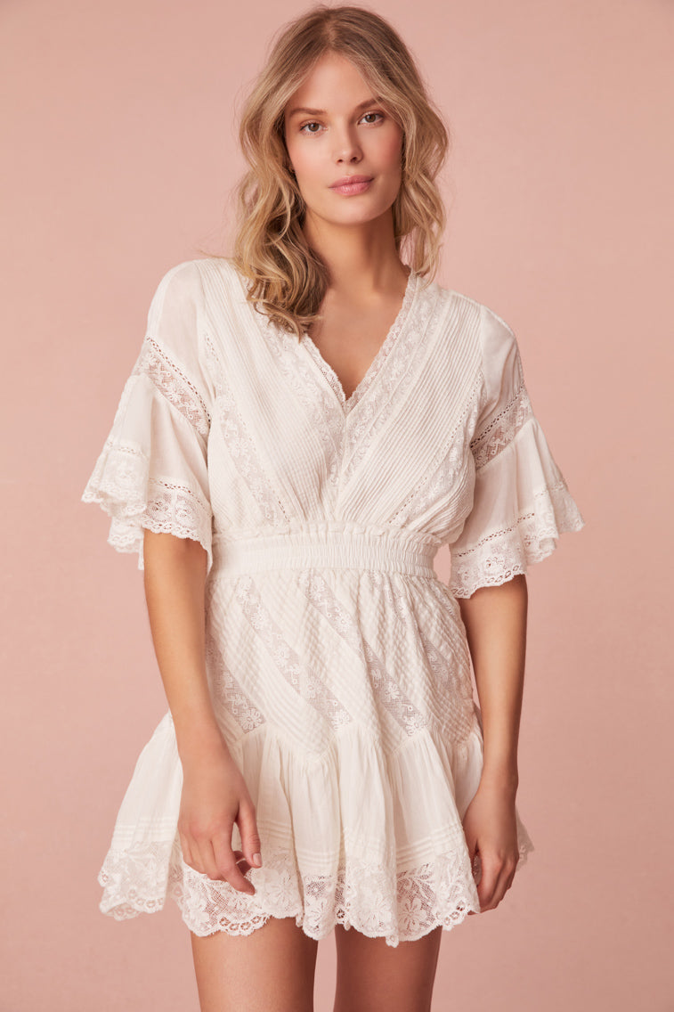 Mini dress featuring laces and pintuck details. Begins with short flowy sleeves, a v-neckline that falls to an elasticated waistband which releases into an airy skirt.
