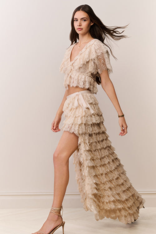 Woman wearing a beige ruffled outfit against a plain background