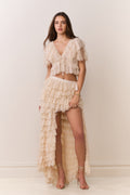 Woman wearing a beige ruffled outfit against a plain background