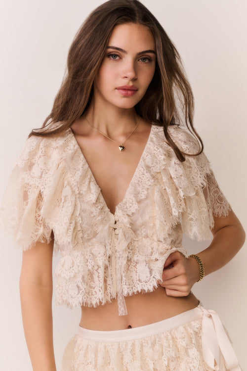 Woman wearing a beige lace top against a plain background
