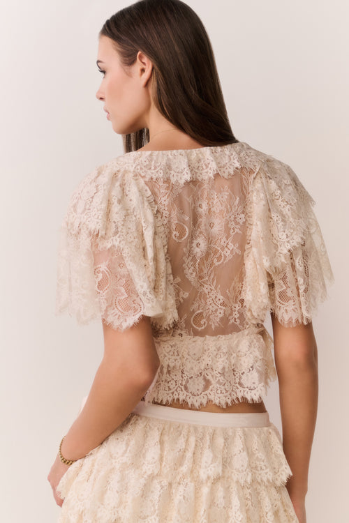 Woman wearing a lace top and skirt set against a plain background