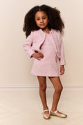 Young girl wearing a pink outfit with a matching jacket and skirt against a plain background
