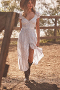 Woman in a blue floral dress and cowboy boots standing in a rural setting.