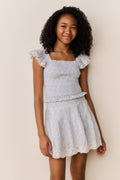 Young girl wearing Light blue floral pattered skirt with lace trim and matching shirt with ruffled details on a beige background