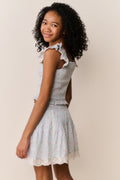 Young girl wearing Light blue floral pattered skirt with lace trim and matching shirt with ruffled details on a beige background