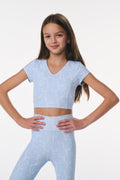 Young girl wearing a light blue athletic outfit with a pattern on a white background
