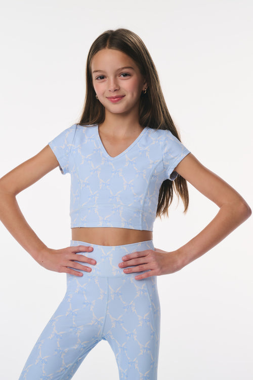 Young girl wearing a light blue athletic outfit with a pattern on a white background
