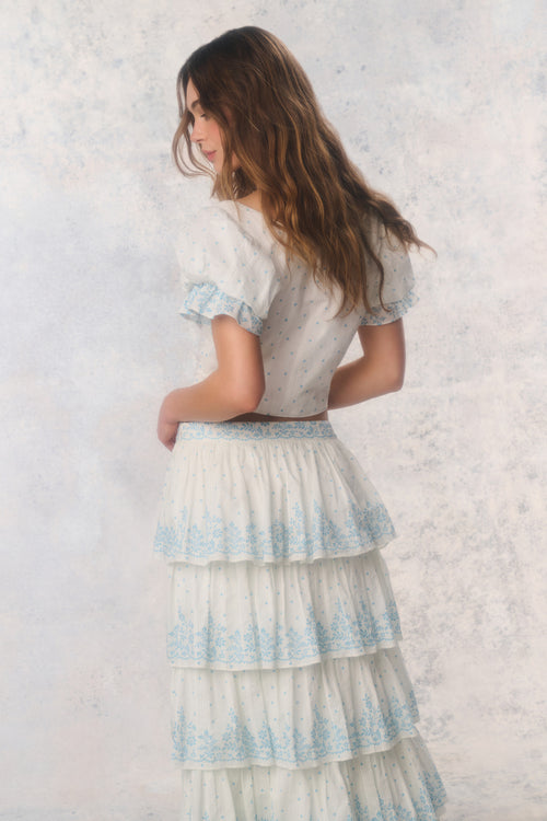 Woman wearing a layered dress with blue patterns against a textured white background