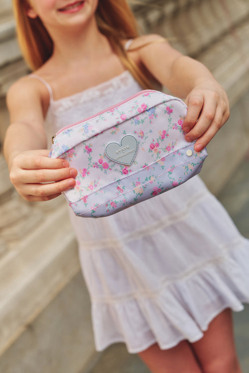 Young girl holding a floral pouch with a heart emblem.
