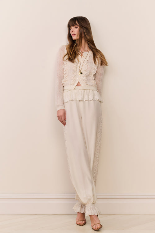 Woman wearing a cream-colored outfit with ruffled details against a plain background