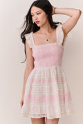 Woman wearing pink and white dress with lace details on a plain background